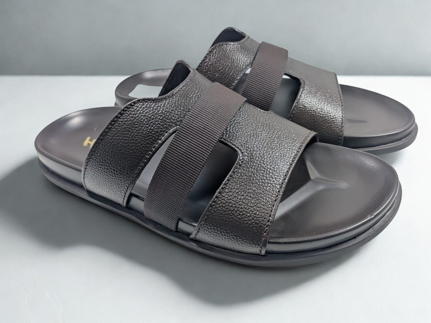 Pair of dark gray sandals with strap details on a light gray background