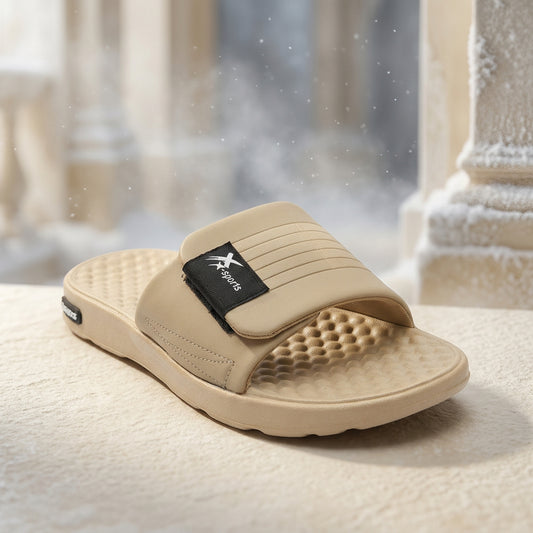 A single beige slide sandal with a textured footbed and a black strap label featuring a white logo, photographed on a clean white background.
