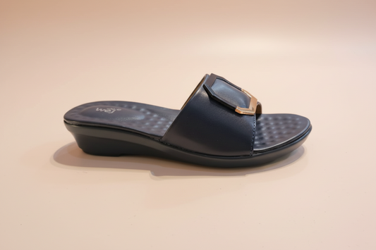 Black sandal with a gold buckle on a light-colored floor.