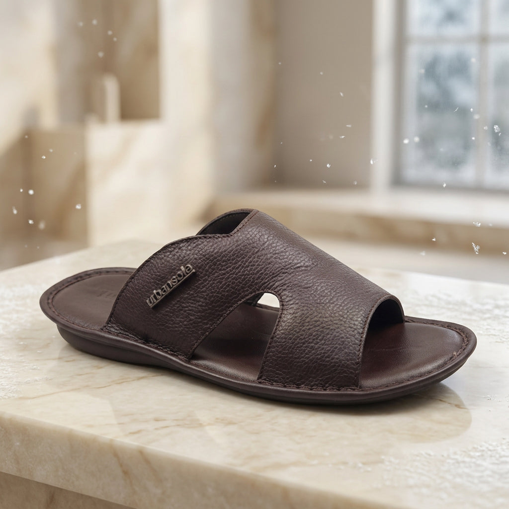 A dark brown leather slide sandal with a textured pebbled upper strap and a contoured footbed, shown from a three-quarters angle on a white background.