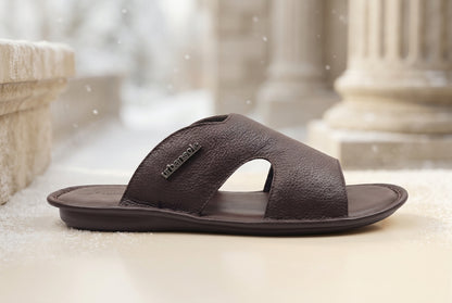 A dark brown textured leather slide sandal with a cutout design and a small 'urbanwalk' brand tag on the side, shown against a plain light gray background.