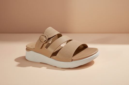 Brown sandal with a white sole on a light-colored floor.