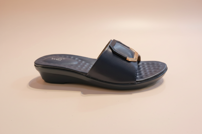 Black sandal with a gold buckle on a light-colored floor.